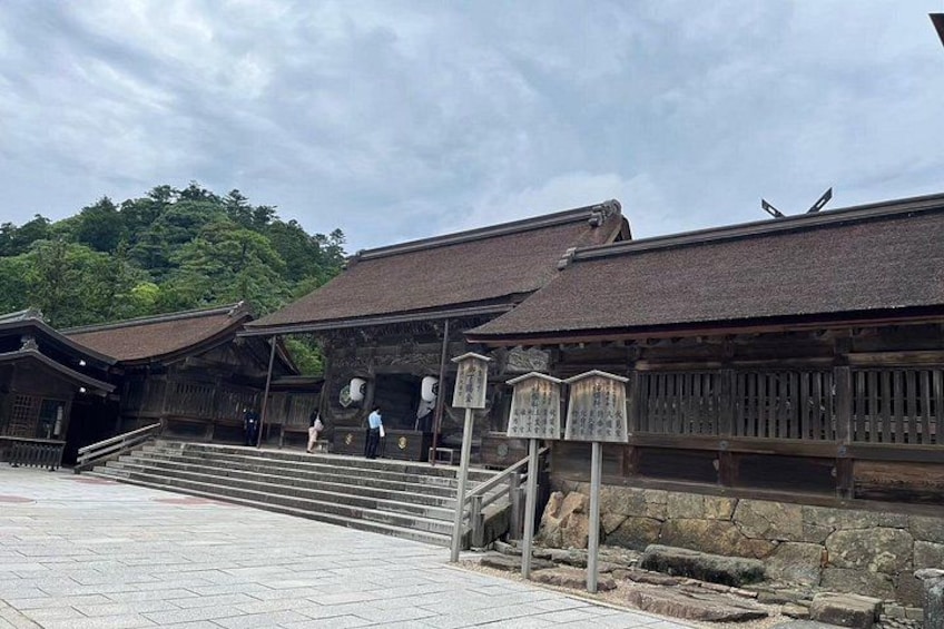 Un bâtiment traditionnel japonais, avec un toit recouvert de tuiles et des murs en bois, entouré d’escaliers en pierre et d’une zone pavée. 4