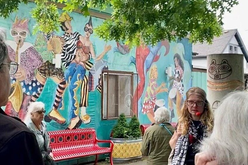 A mural with colorful characters, a red bench, and a tree. 2