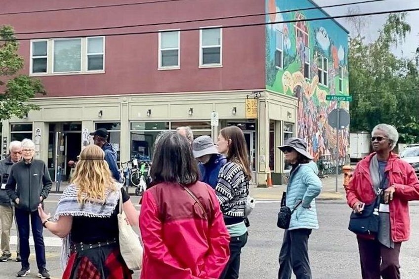 Un grupo de personas está de pie en una calle frente a un edificio con un mural colorido. 1