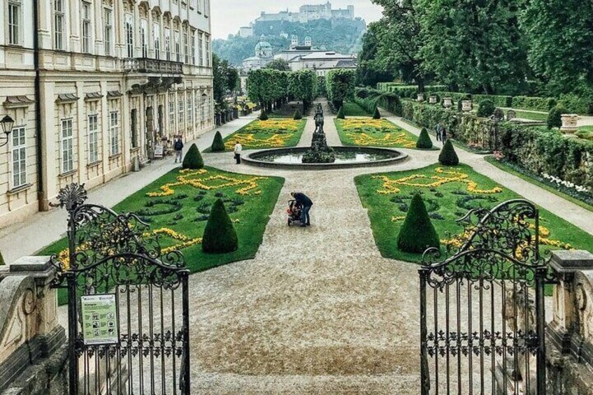 Un jardín formal con parterres geométricos, una fuente central y un edificio grande a la izquierda. 2