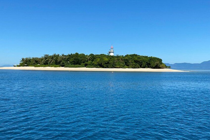 A lighthouse on a small island surrounded by clear blue water. 1