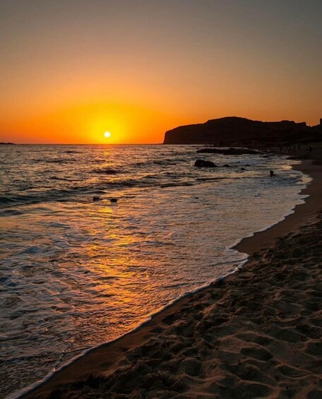 Ein Sonnenuntergang über einem Strand mit Wellen und einem entfernten Berg. 2