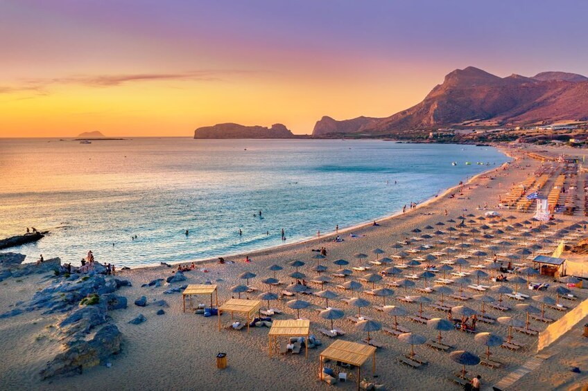 Ein Strand mit Sonnenschirmen und Liegestühlen, ein ruhiges Meer und Berge im Hintergrund. 1
