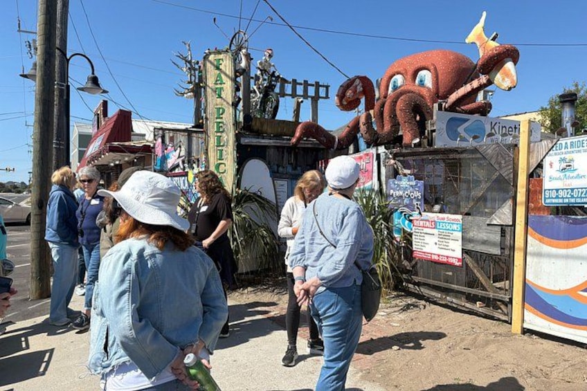 A street scene with a large octopus mascot, people walking, and a sign for a ridesharing service. 2