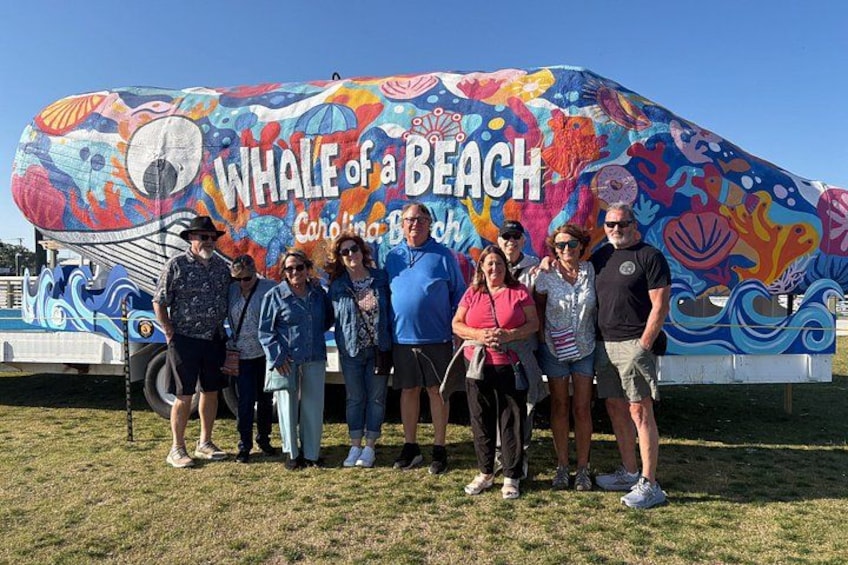 A group of people standing in front of a colorful mural titled 'Whale of a Beach' with a beach theme. 5