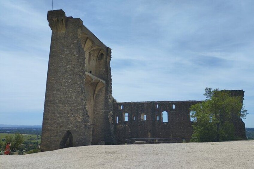 A ruined stone tower and building with arched openings, surrounded by a gravel area and trees. 5