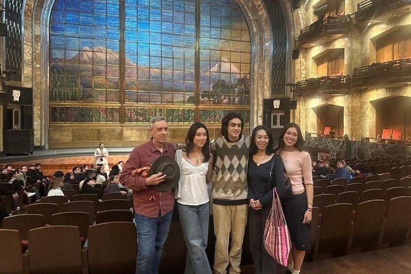 A group of people standing in an auditorium with a large arched window and a stage. 3