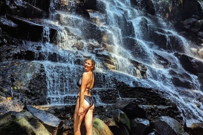 A woman in a bikini standing in front of a waterfall. 3