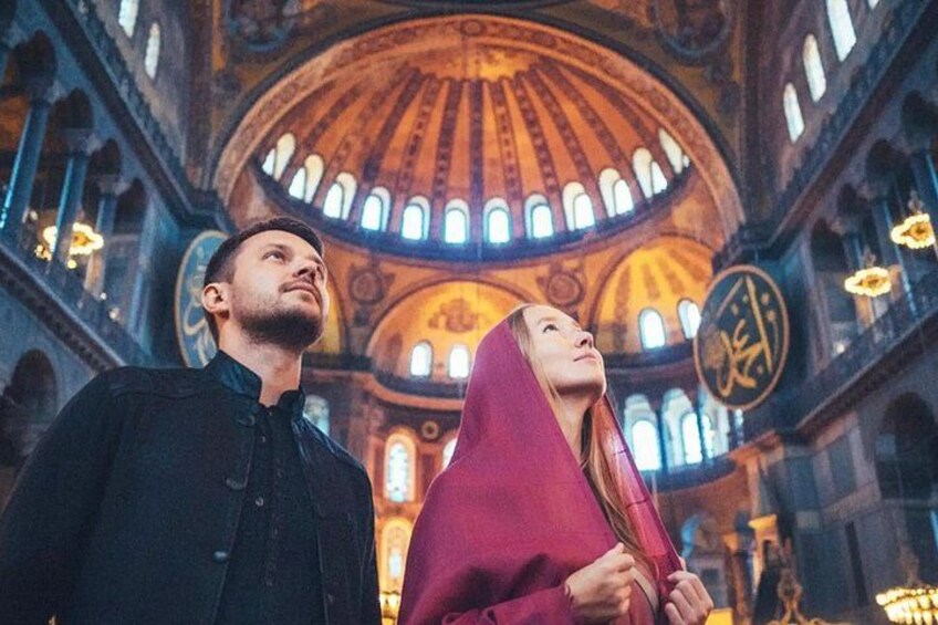 A man and a woman in traditional attire inside a grand building with a large dome and arched windows. 4
