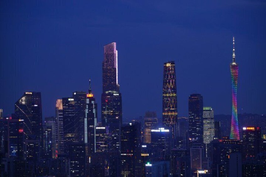 A city skyline at night with illuminated skyscrapers and a prominent tower with a rainbow light display. 5
