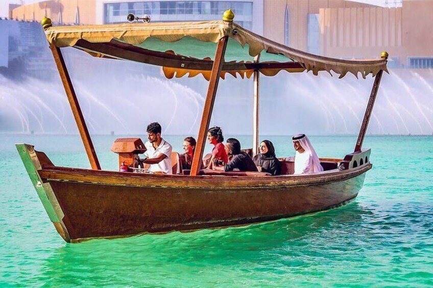 A traditional wooden boat with passengers on turquoise water, with a fountain in the background. 2