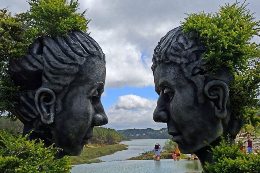 Two statues with trees on their heads, a river, and a person in the background. 3