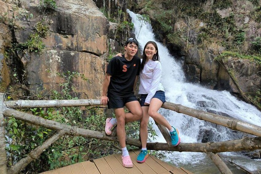 Two people sitting on a wooden bridge with a waterfall in the background. 2
