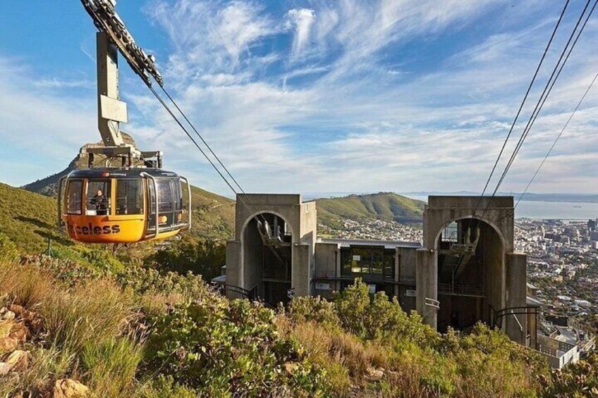 A cable car system with a yellow cable car labeled "Cableless" suspended by cables, overlooking a city and hills. 3