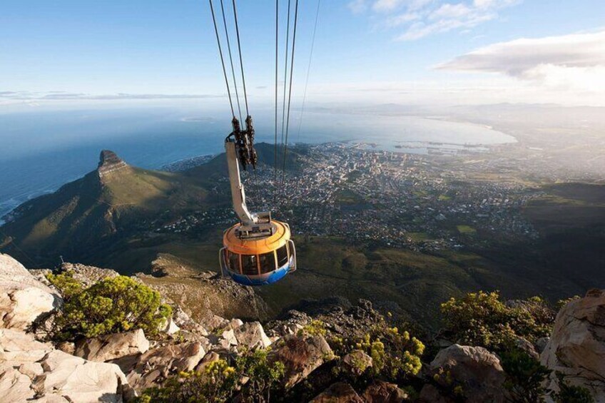 A cable car ascending a mountain with a city and coastline in the background. 2