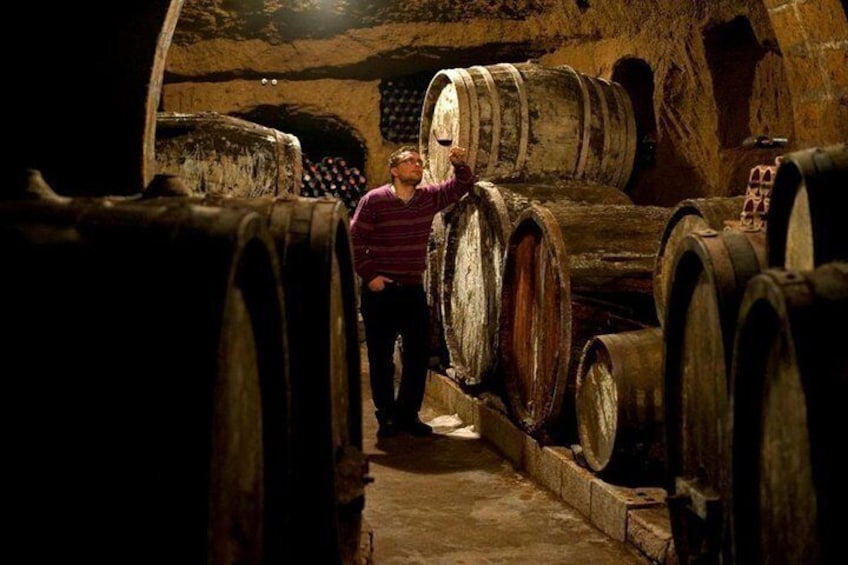Una cantina scarsamente illuminata con botti di legno e una persona che le esamina. 1