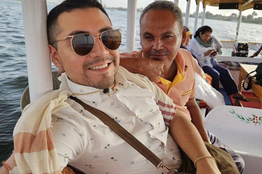 A person wearing a patterned shirt and sunglasses, seated on a boat with a white tablecloth and a floral design. 2