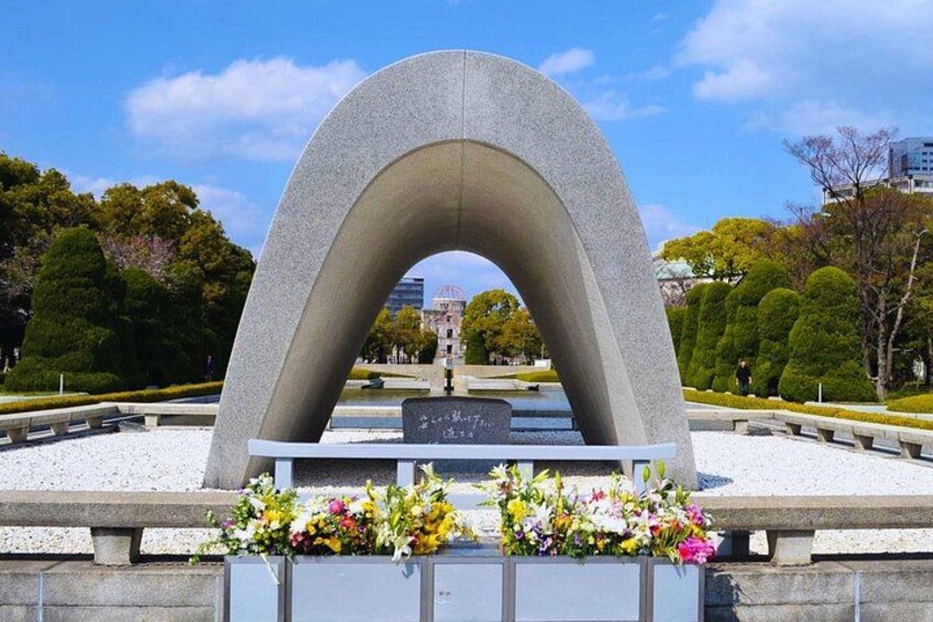 Een stenen monument met een bogenpoort, omringd door een park met bomen en een fontein. 4