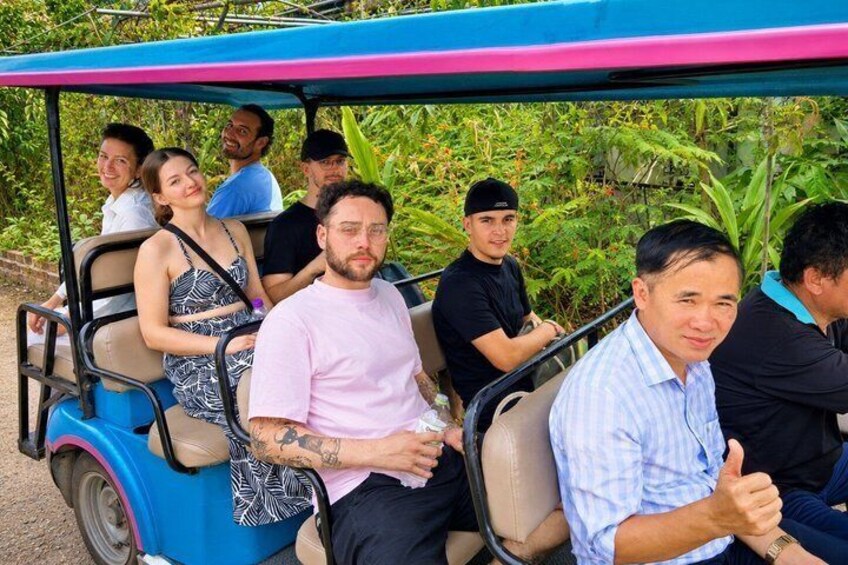 A group of people on a golf cart in a lush, green environment. 1