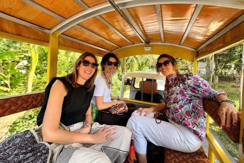 Three people seated inside a vehicle with a wooden interior, surrounded by greenery. 5
