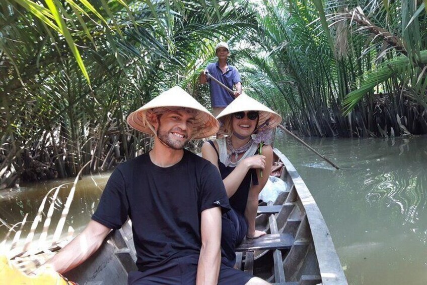 Two people in a boat with a woman wearing a conical hat, surrounded by dense mangrove vegetation. 1