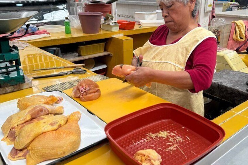 A person preparing food with raw chicken on a yellow counter, surrounded by kitchen utensils and a red tray. 2