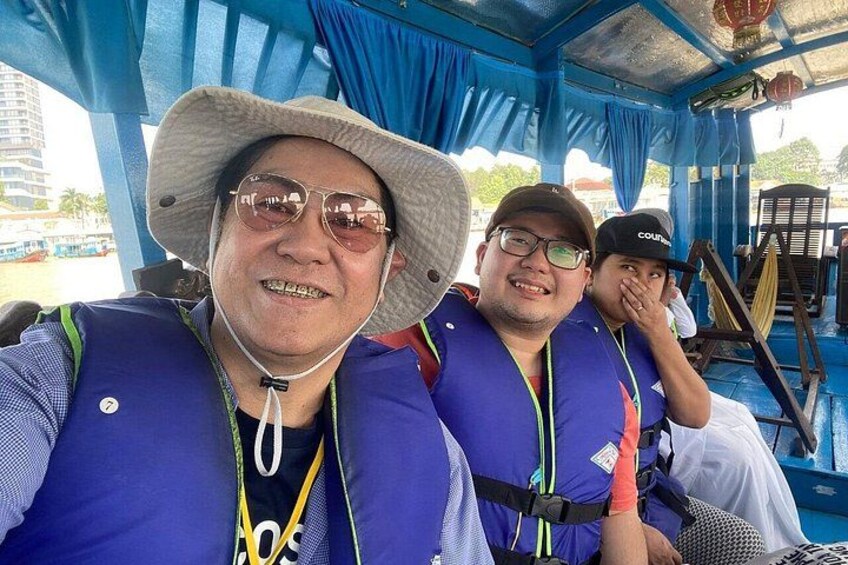 A person wearing a blue life jacket and a hat, seated on a boat with blue curtains. 2