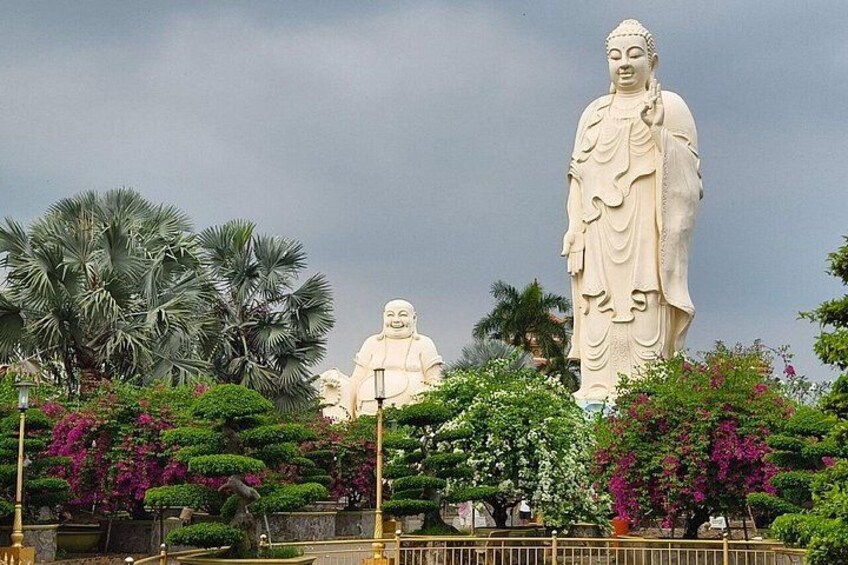 Large white Buddha statues surrounded by lush greenery and flowering plants. 4