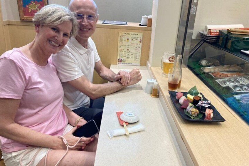 To personer sidder ved en disk med en menutavle, et glas øl og en tallerken sushi. 4