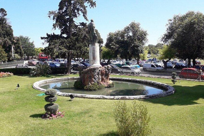 A park with a fountain, trees, and a parking lot in the background. 5