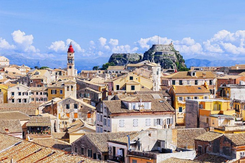 A coastal town with historic buildings, a prominent clock tower, and a fort on a hill. 4