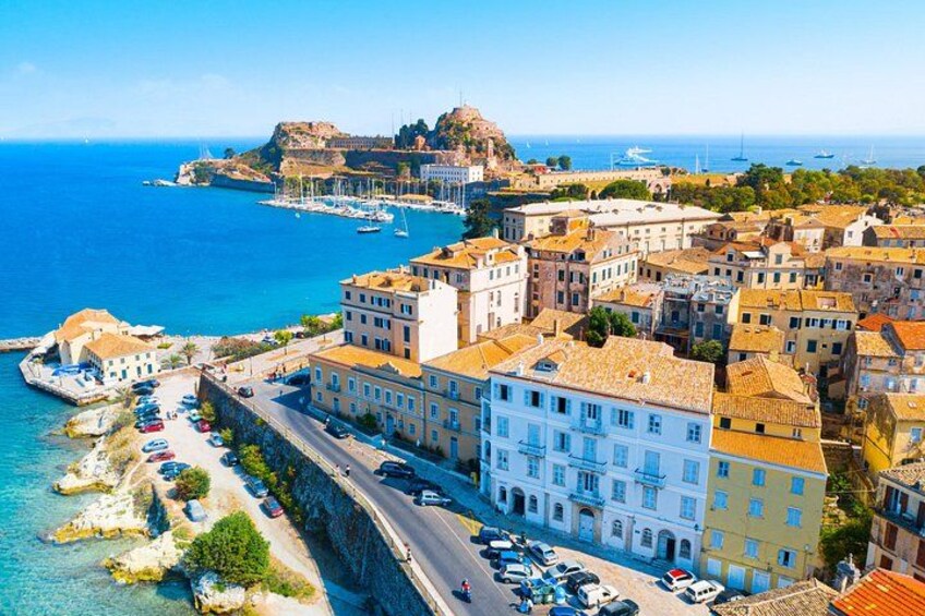 A coastal town with historic buildings, a fortified structure, and a clear blue sea. 2