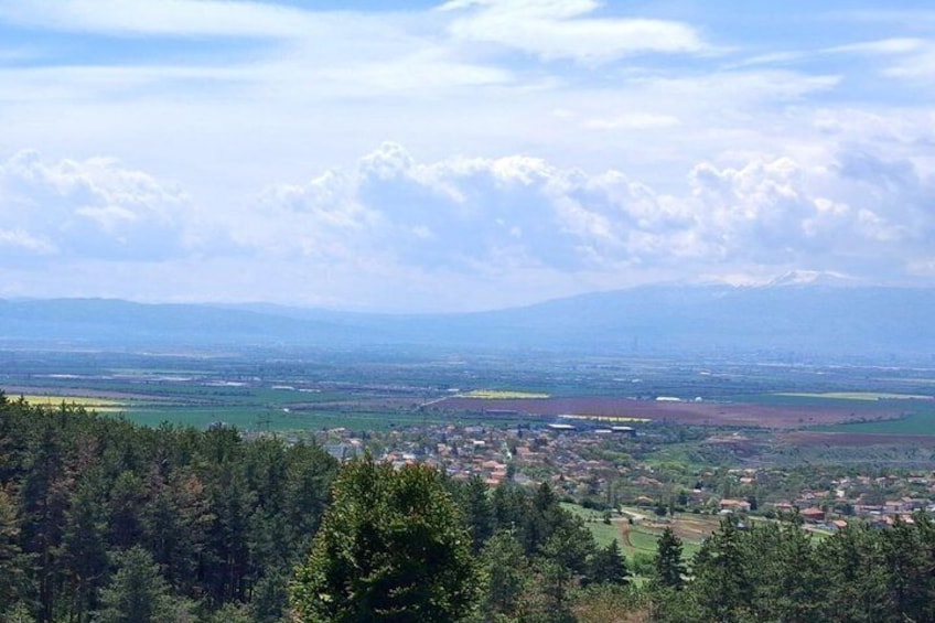 A mountainous landscape with a town in the valley, dense forests, and a clear sky. 4