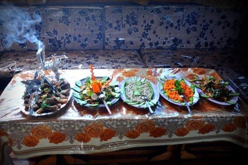 A table with various dishes, a smoking hookah, and a patterned wall in the background. 2