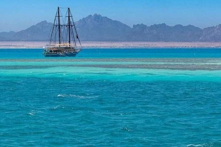 A sailing boat on turquoise waters with a mountainous coastline in the background. 4
