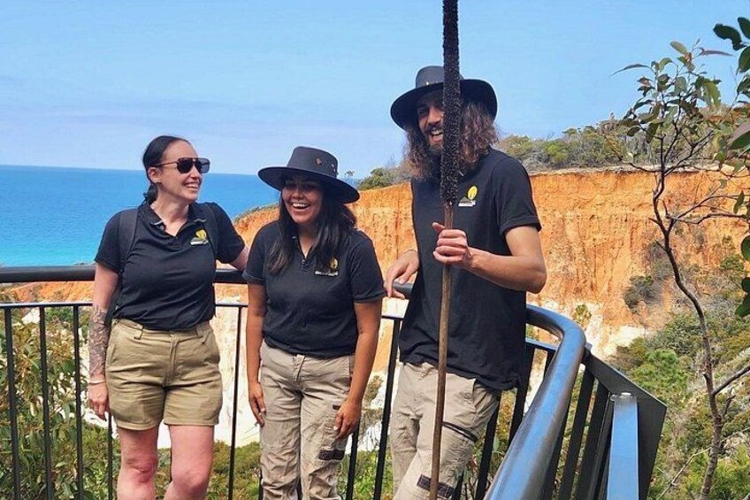 Three people standing on a railing overlooking a coastal landscape with cliffs and the ocean. 1