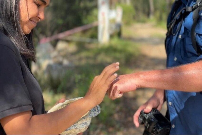 A person holding a camera, another person extending a hand, and a natural outdoor setting with rocks and greenery. 3