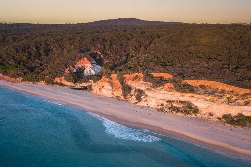 A coastal landscape with a beach, cliffs, and forested hills. 4