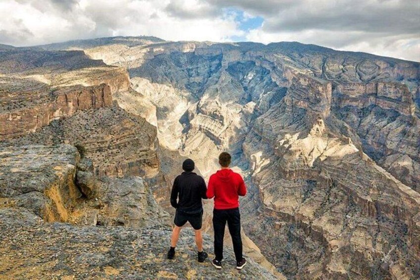 Two people standing on a rocky outcrop overlooking a canyon with layered rock formations. 4