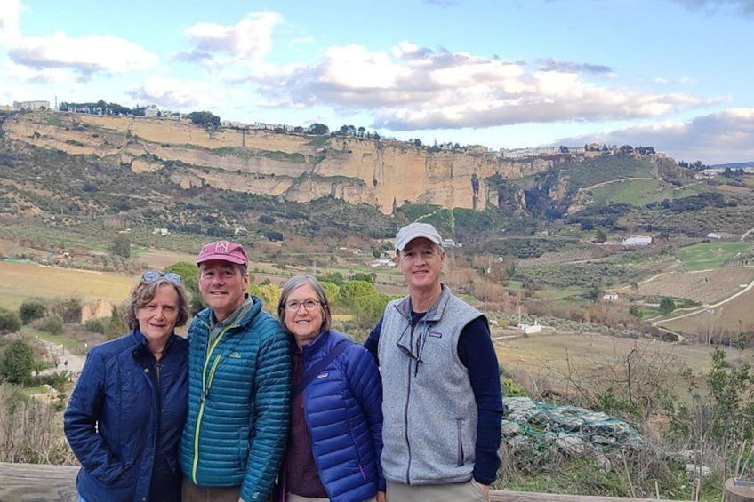 A group of people standing on a wooden deck with a scenic view of a valley and cliffs in the background. 2
