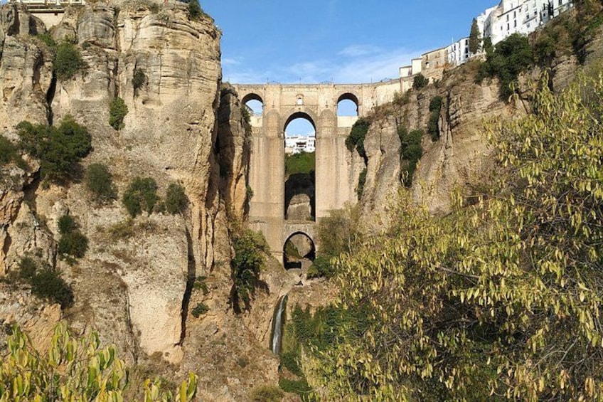 A historical stone bridge with arches, a rocky cliff, and a pathway leading to it. 5