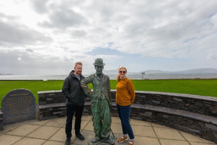 A statue of a man in period clothing, a plaque with text, and a grassy area with a stone wall and a view of the sea. 3