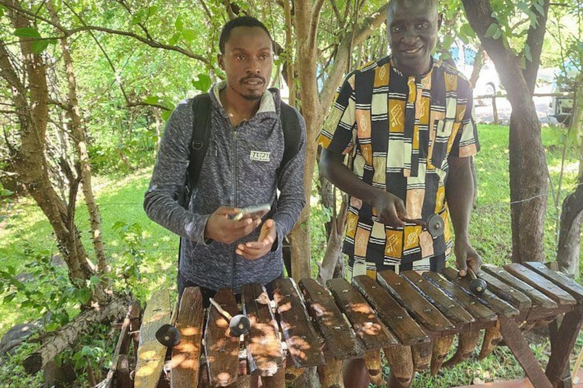 Two people standing by a wooden structure with musical instruments. 1