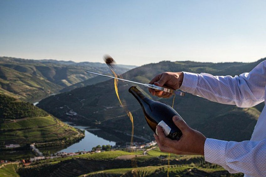 Una persona tiene una bottiglia di vino con un vigneto e un fiume sullo sfondo. 1