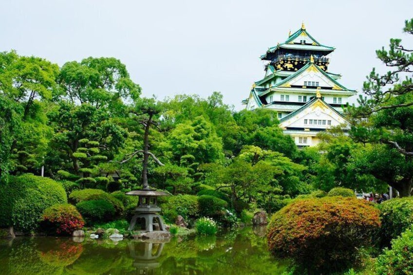 Un castillo japonés tradicional rodeado de exuberante vegetación y un estanque con una pagoda. 1