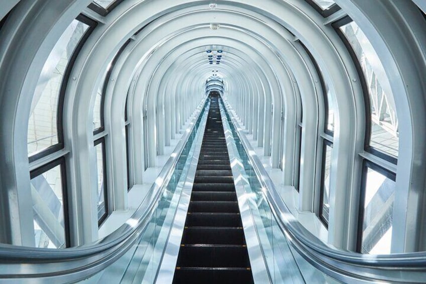Una escalera mecánica en un edificio moderno con un pasillo curvo y paredes de vidrio. 5