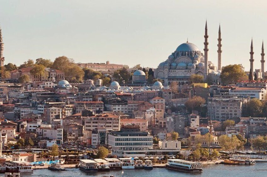 A cityscape with a prominent mosque with blue domes and minarets, dense urban buildings, and a river with boats. 4