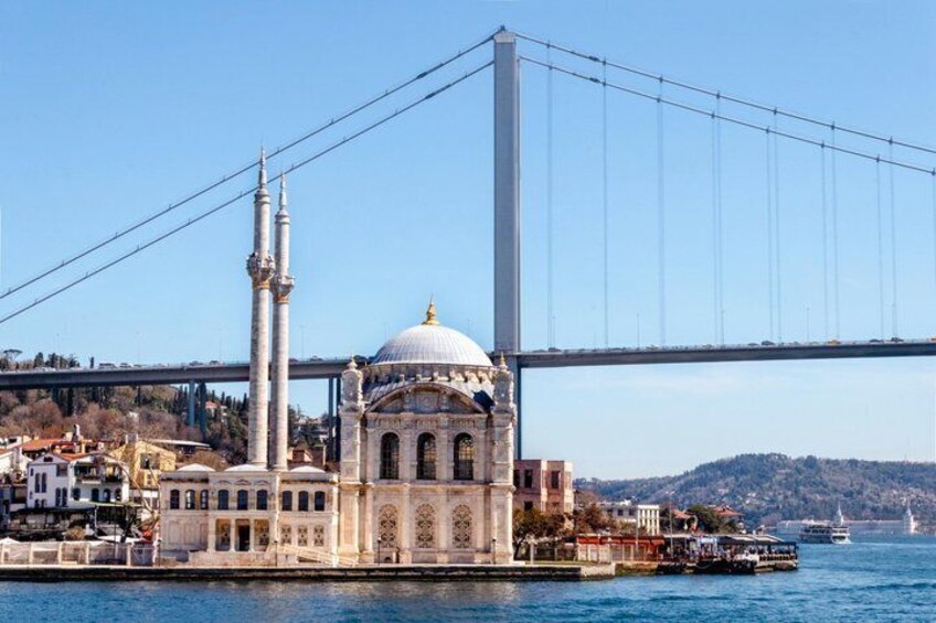 A mosque with a large dome and minarets, a bridge in the background, and a body of water. 1