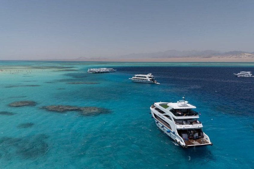 A large yacht anchored in clear turquoise waters with a sandy beach and distant mountains in the background. 1