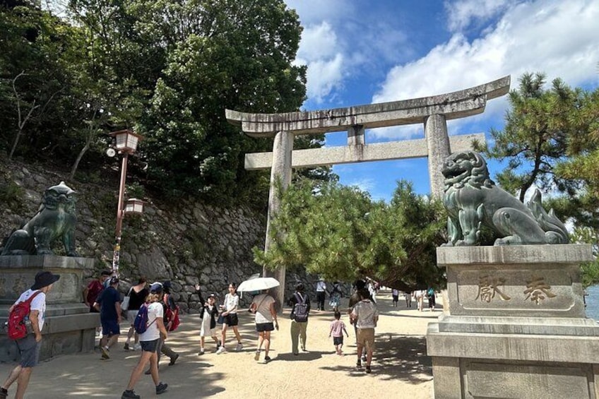 En port av sten i form av en torii, en staty av en stenlejon och människor som promenerar i en park. 5
